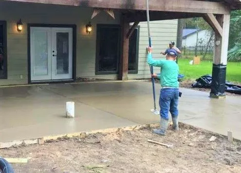 Worker smoothing a fresh concrete patio behind a home in Tomball, TX